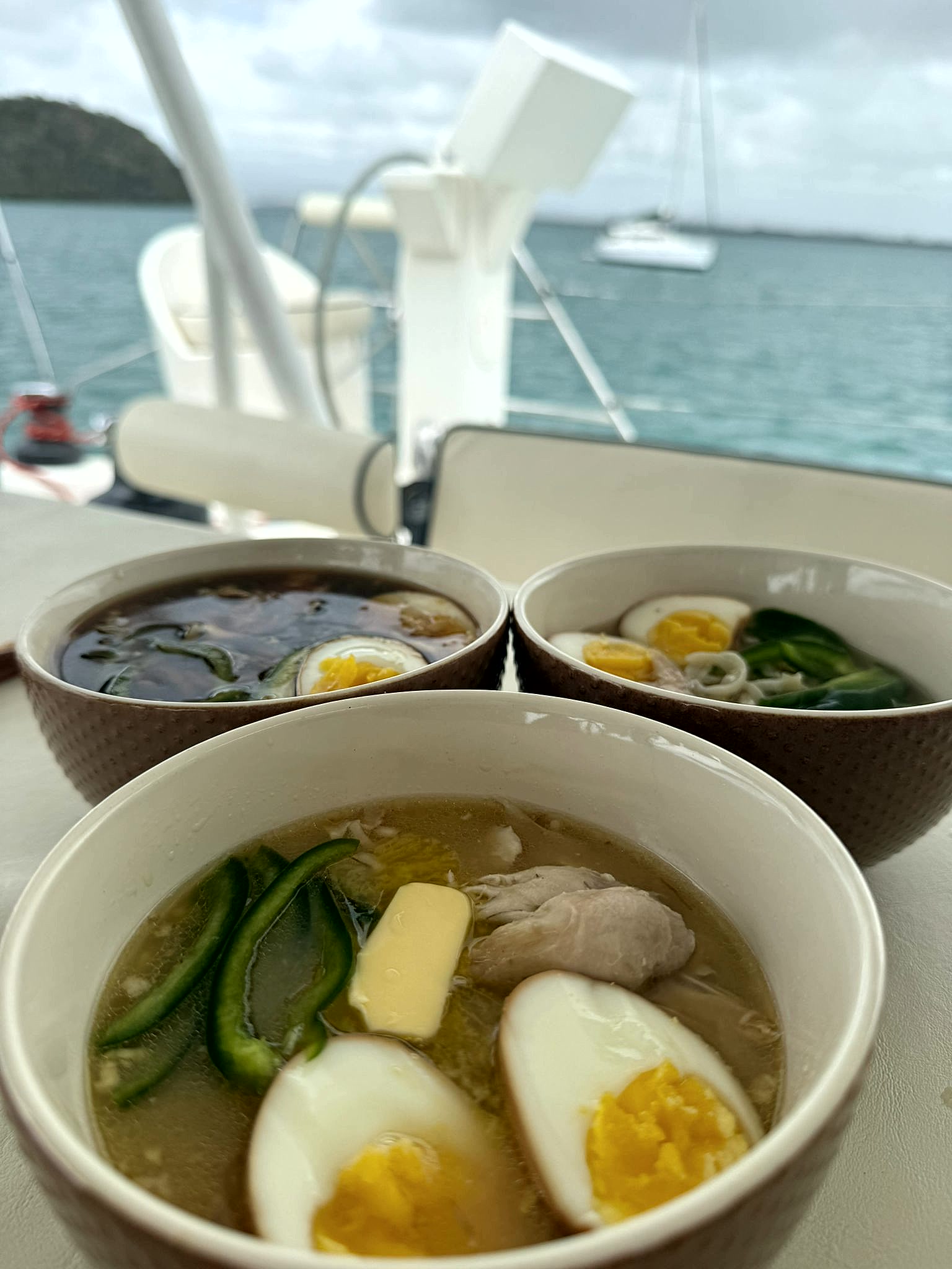 Three bowls of house-made chicken ramen with soft-boiled egg, served on the deck of a catamaran at anchor in the BVI